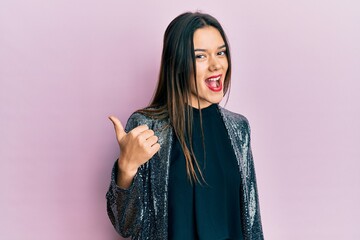 Wall Mural - Young hispanic girl wearing party jacket smiling with happy face looking and pointing to the side with thumb up.