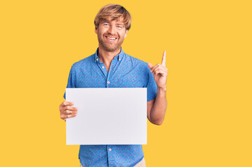 Poster - Handsome caucasian man with beard holding sale poster surprised with an idea or question pointing finger with happy face, number one