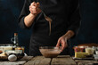 Pastry chef testing dough with a spoon. Backstage of cooking waffle on rustic wooden table with ingredients on dark blue background. Frozen motion. Handmade dessert. Cooking process.