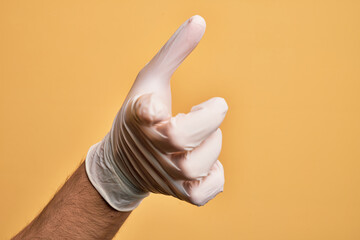 Wall Mural - Hand of caucasian young man with medical glove over isolated yellow background pointing forefinger to the camera, choosing and indicating towards direction