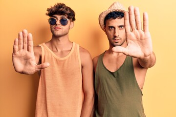 Wall Mural - Young gay couple wearing summer clothes doing stop sing with palm of the hand. warning expression with negative and serious gesture on the face.