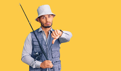 Wall Mural - Handsome latin american young man wearing fisherman equipment with angry face, negative sign showing dislike with thumbs down, rejection concept