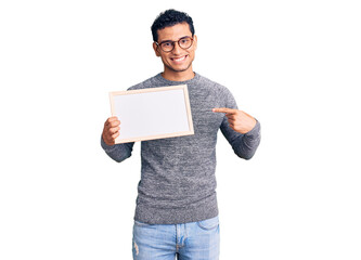 Wall Mural - Hispanic handsome young man holding blank empty banner smiling happy pointing with hand and finger