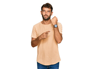 Poster - Handsome young man with beard wearing casual tshirt in hurry pointing to watch time, impatience, looking at the camera with relaxed expression