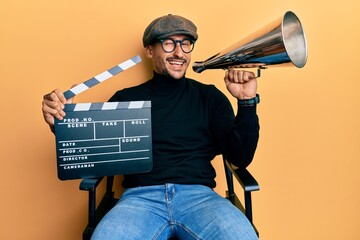 Sticker - Handsome man with tattoos holding video film clapboard and louder winking looking at the camera with sexy expression, cheerful and happy face.