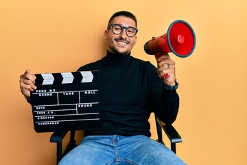 Sticker - Handsome man with tattoos holding video film clapboard and megaphone smiling with a happy and cool smile on face. showing teeth.