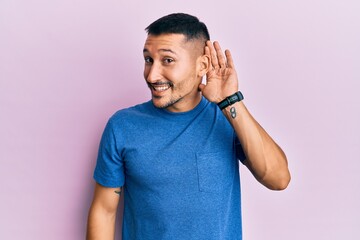 Poster - Handsome man with tattoos wearing blue tshirt clothes smiling with hand over ear listening and hearing to rumor or gossip. deafness concept.