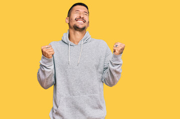 Poster - Handsome man with tattoos wearing casual sweatshirt very happy and excited doing winner gesture with arms raised, smiling and screaming for success. celebration concept.