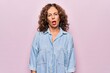 © Krakenimages.com - Middle age beautiful woman wearing casual denim shirt standing over pink background In shock face, looking skeptical and sarcastic, surprised with open mouth