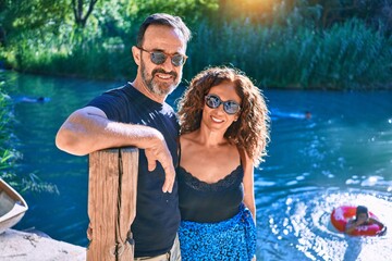 Wall Mural - Middle age couple wearing casual clothes smiling happy. Standing looking at the camera hugging around river at park