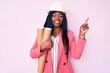 © Krakenimages.com - Young african american woman wearing architect hardhat holding blueprints smiling happy pointing with hand and finger to the side