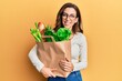 © Krakenimages.com - Young brunette woman holding paper bag with bread and groceries looking positive and happy standing and smiling with a confident smile showing teeth