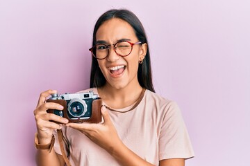 Sticker - Young asian woman holding vintage camera winking looking at the camera with sexy expression, cheerful and happy face.