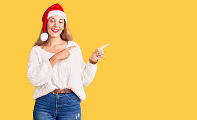 Sticker - Beautiful young woman wearing christmas hat smiling and looking at the camera pointing with two hands and fingers to the side.