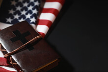 American Flag And Holy Bible Book On A Mirror Background. Symbol Of The United States And Religion. Bible And Striped Flag On A Black Background.