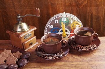 Coffee time. Clock face, two cups of coffee with saucers, a saucer with sweets and cookies on a wooden table.