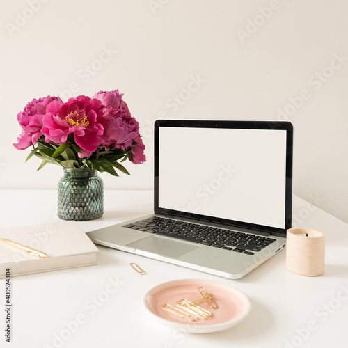 Office desk table workspace with blank copy space mock up laptop screen. Modern stylish home interior design with pink peonies flower bouquet. Blog, social media, website hero template.