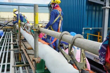 Hook of safety harness on scaffolding pipe during working at heights in construction site, Chemical plant.