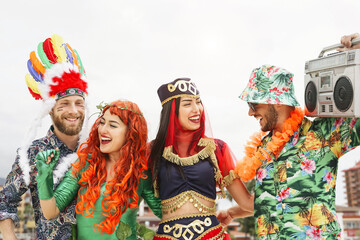 Happy friends celebrating carnival party outdoor - Young crazy people having fun wearing costumes listening music with vintage boombox stereo - Youth holidays culture lifestyle concept