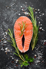 Salmon steak and ingredients on black stone background. Top view. Free space for your text.