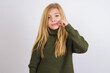 Caucasian kid girl wearing green knitted sweater against white wall mouth and lips shut as zip with fingers. Secret and silent, taboo talking.