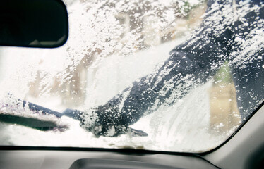 Wall Mural - Male driver in gloves brushes car windshield from snow - view from interior