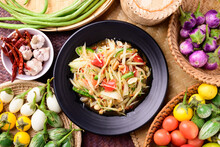 Thai Food (Som Tum), Spicy Green Papaya Salad With Vegetables On Woven Bamboo Background, Top View