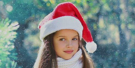 Christmas portrait of happy smiling little girl child in santa red hat outdoors