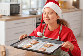 Sticker - Young woman baking tasty gingerbread cookies in kitchen on Christmas eve