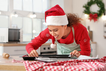 Sticker - Young woman baking tasty gingerbread cookies in kitchen on Christmas eve