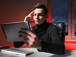 Poster - A focused man sits in his office and holds a tablet PC in his hands. The analyst studies stock information. Remote work during the pandemic. A man reads news related to his business.
