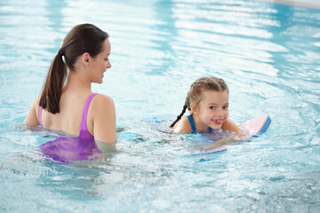 Wall Mural - Happy young brunette woman helping adorable little daughter to swim in pool