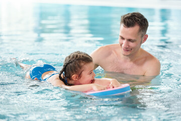 Wall Mural - Happy young father teaching his little daughter to swim in pool in spa center