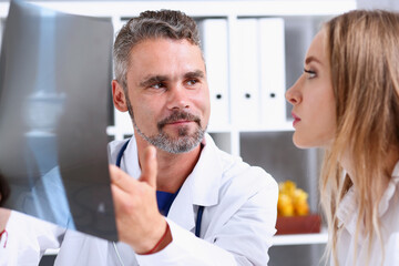 Wall Mural - Mature male doctor hold in arm and look at xray photography discussing it with female patient portrait. Bone disease exam, medic assistance, cancer test, healthy lifestyle, hospital practice concept