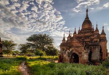 Wall Mural - Ancient Buddhist pagoda against cloudy sky in the old city of Bagan, the world heritage site in Myanmar (Burma). Carriages with tourists in the background.