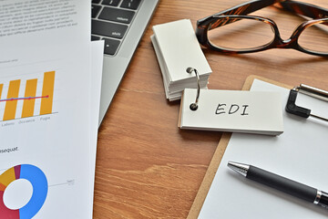 Poster - There is a piece of paper with a graph printed on it, a clipboard, and an open vocabulary book on the desk. The word EDI is there. It's an acronym that means Electronic Data Interchange.
