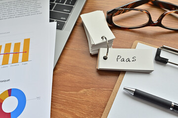 Poster - There is a piece of paper with a graph printed on it, a clipboard, and an open vocabulary book on the desk. The word PaaS is there. It's an acronym that means Platform as a Service.
