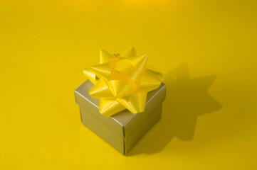 grey gift box with yellowribbon on yellow background, copy space, flat lay.