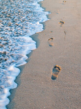 Waves Of Sea Foam Washing Away The Footprints On The Beach Sand In The Morning. 
