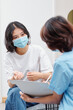 © DragonImages - Young Vietnamese woman in medical mask talking to dental clinic nurse filling document