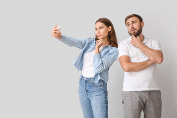 Wall Mural - Young couple taking selfie on light background