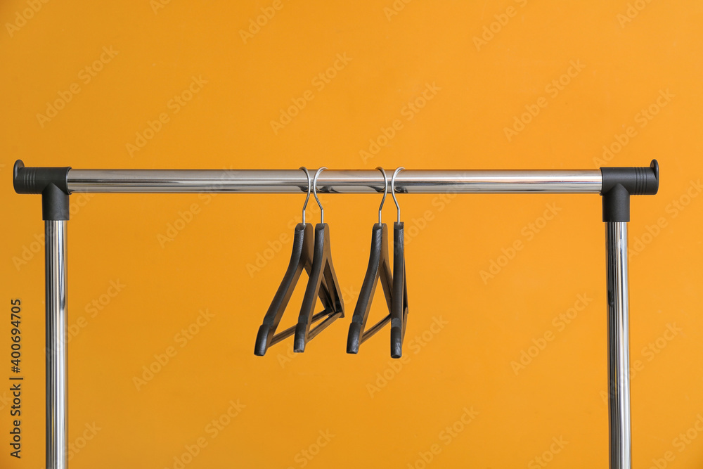 Rack with clothes hangers on color background