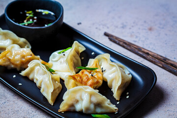 Fried gyoza dumplings with sauce and green onions on black plate, dark background. Japanese cuisine concept.