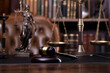 Law and justice theme. Judge chamber. Themis statue, gavel and scale on brown desk. Legal books in the bookshelf as background.