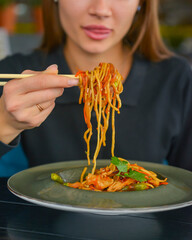 Beautiful young woman eating chinese food called Wok with chopsticks. Wok with meat and fried asparagus in a plate.