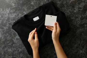 Wall Mural - Female hands hold sweatshirt and blank tag on black table
