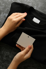 Wall Mural - Female hands hold sweatshirt and blank tag on black table