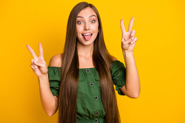 Wall Mural - Portrait of charming funky cheerful brown-haired girl showing v-sign fooling grimacing isolated over bright yellow color background