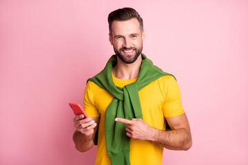 Wall Mural - Photo of sweet cute young man dressed yellow t-shirt sweater shoulders pointing finger modern gadget isolated pink color background