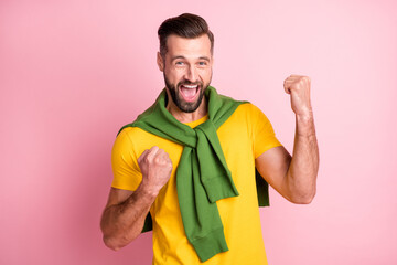 Poster - Photo of cute lucky young guy wear yellow t-shirt pullover shoulders rising fists isolated pink color background